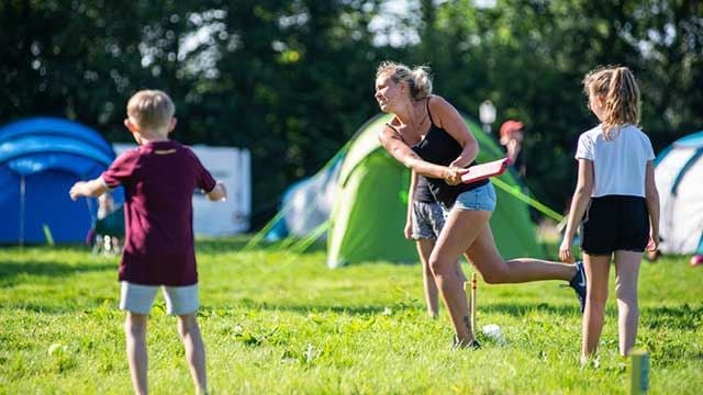 Tents in the background with kids and an adult  playing cricket