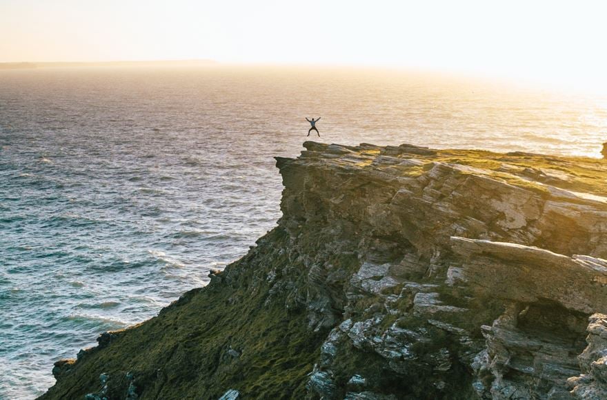  a man jumps in the air at the end of a large rocky cliff overlooking the sea 