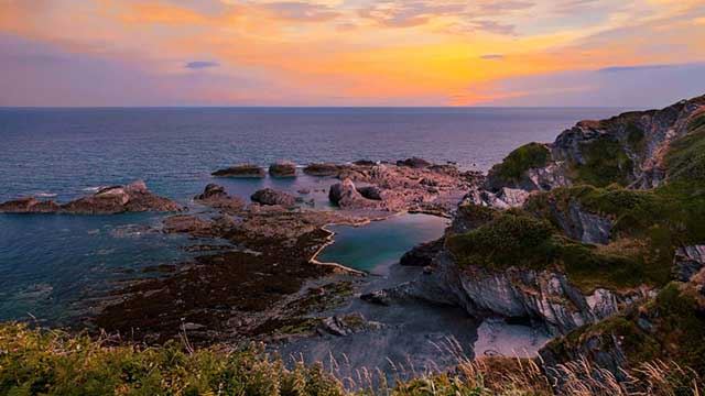 View from the clifftop down to Tunnels Beaches at Ilfracombe with sunset behind