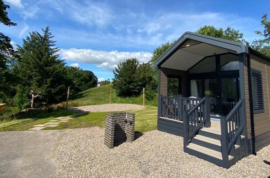 a glamping cabin with a bbq outside, located in a woodlands area 