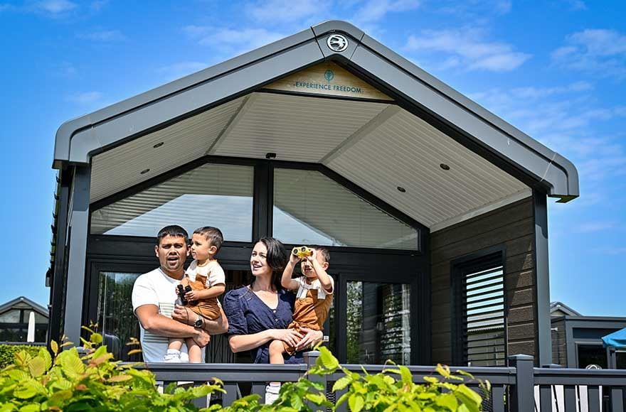 A happy family enjoying the outdoors, standing in front of their glamping cabin and a clear blue sky