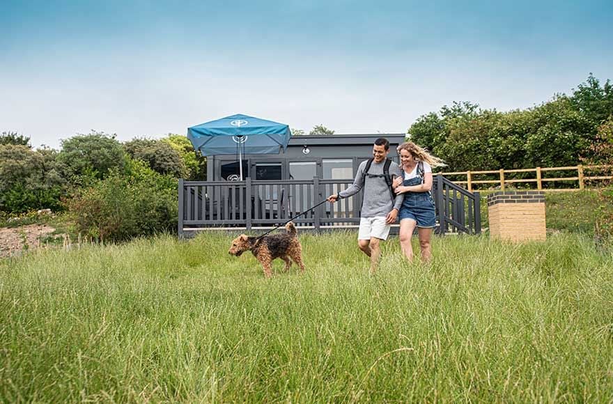 couple walking dog in long grass outside the glamping pod