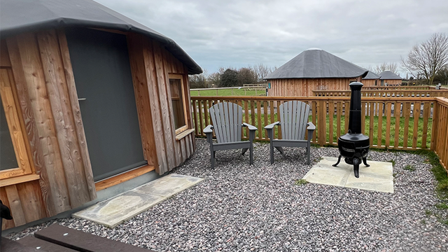 wooden yurt with outdoor seating area and fire pit.