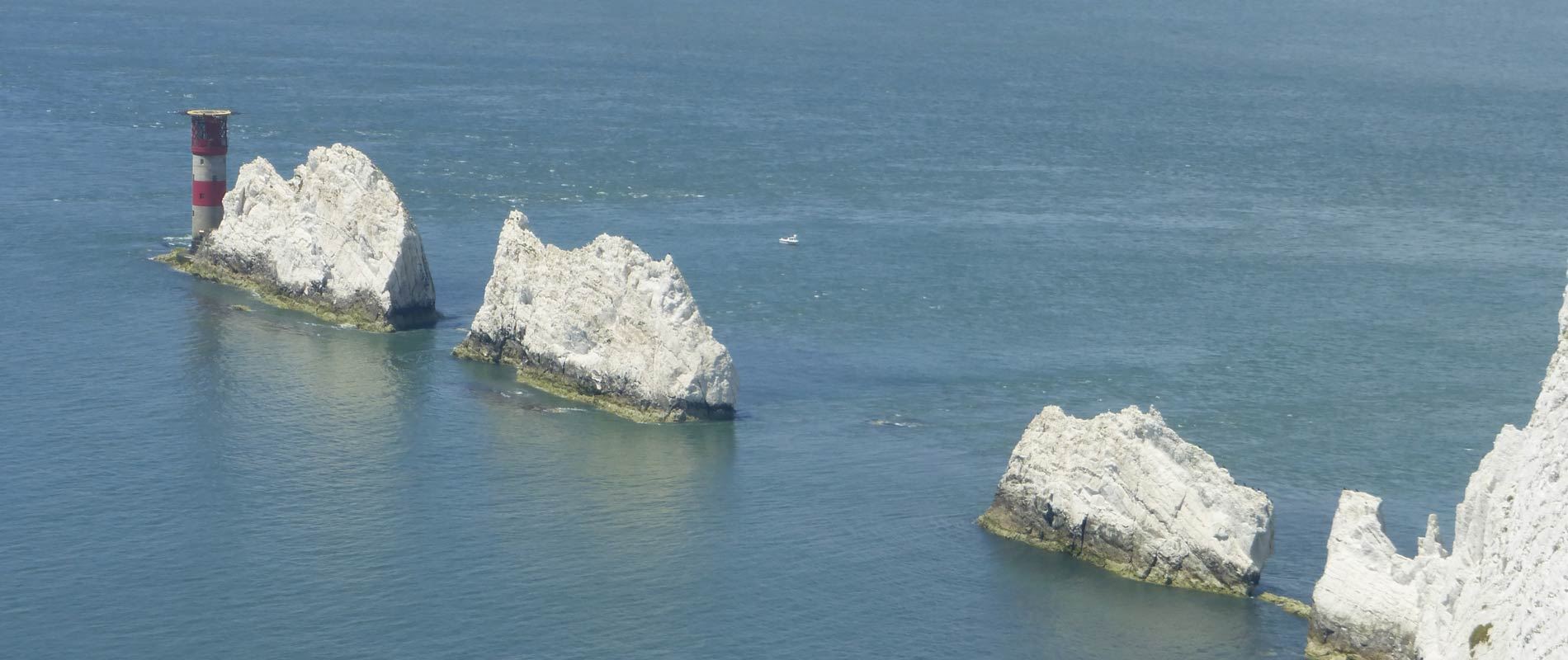 isle of wight white rocks protruding from the sea with a red and white lighthouse  surrounded by a calm blue sea 