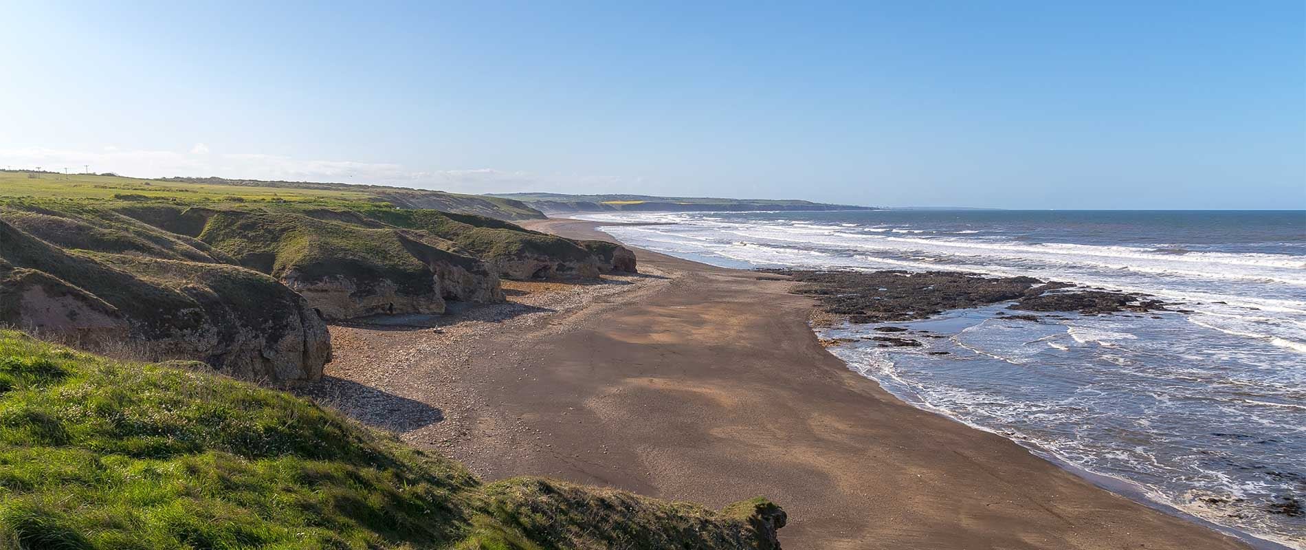 blackhall beach lined by wavey seas and large green hills