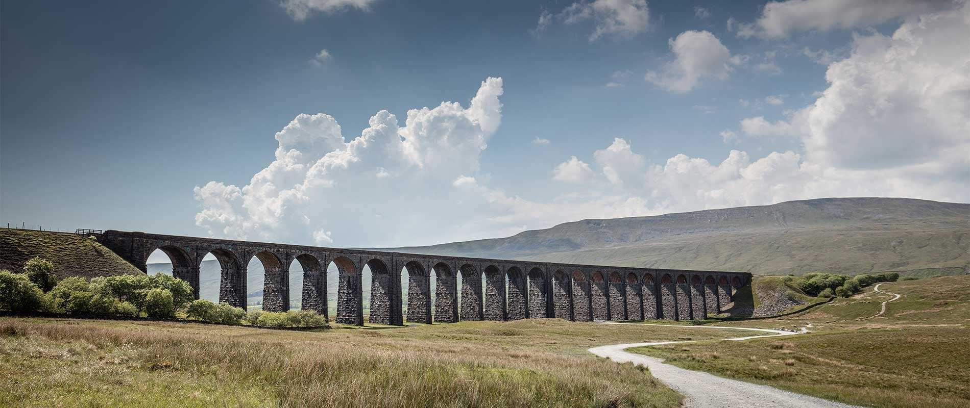 tall stones of ribblehead viaduct against a blue cloudy sky and grassy green field