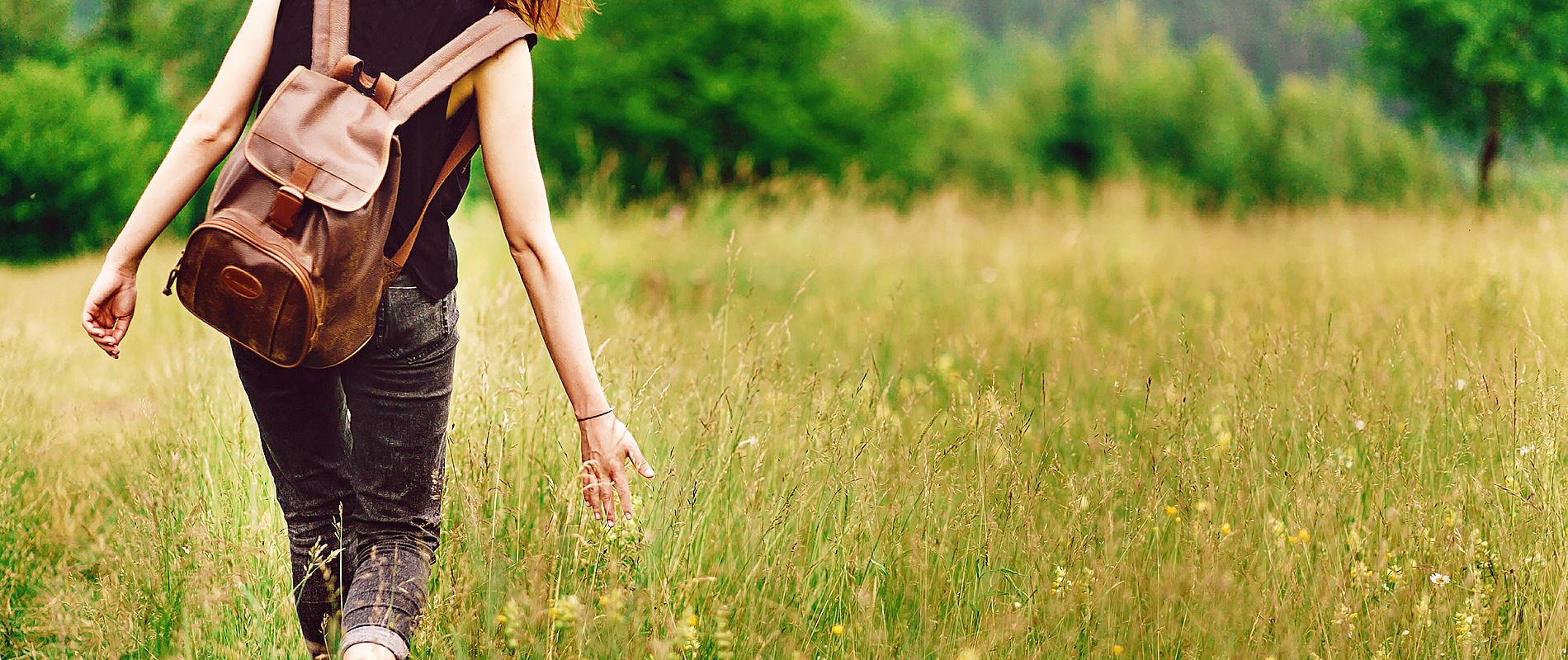 lady wearing backpack walking in a meadow 