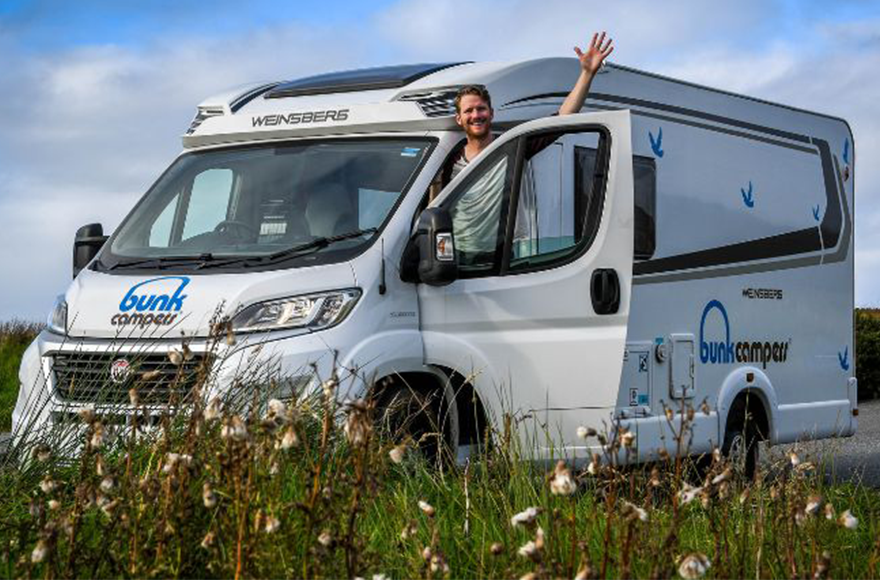 Motorhome parked in a field of flowers with a man waving out the window 