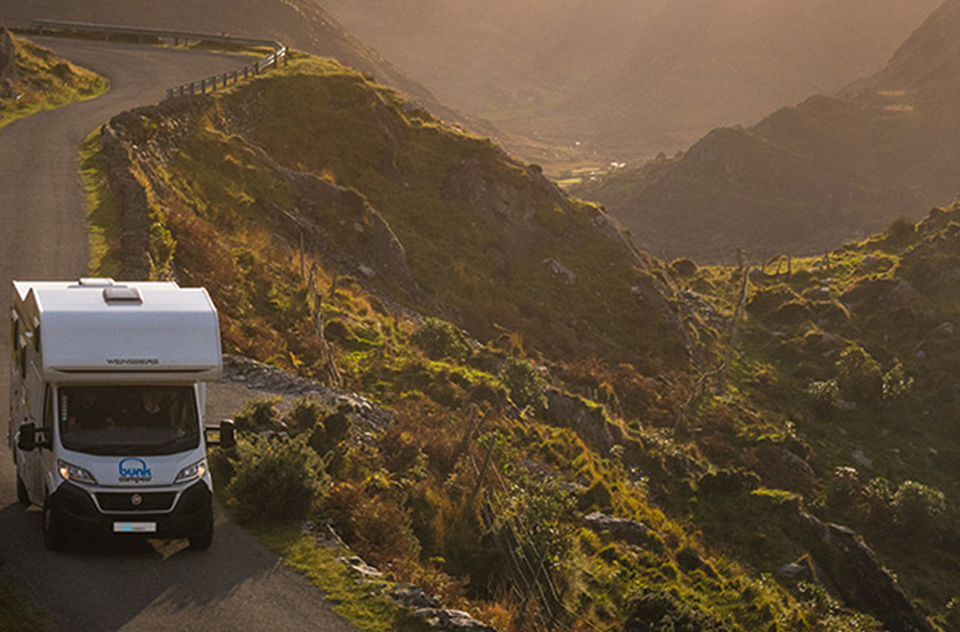 Bunk motorhome driving down a winding road next to a rocky green landscape