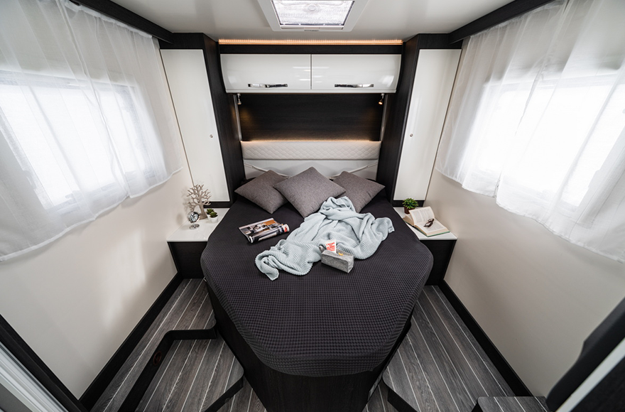 campervan bedroom with bed and cupboard surrounded by windows