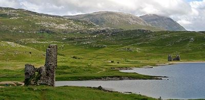 ruins of Ardvreck Castle in green hills and a lake 