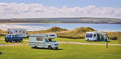 Motorhomes on a gren landscape with Dunnet Bay in the background 