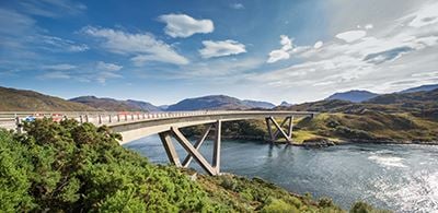 a large bridge over water glistening in the sun lined by green bushes