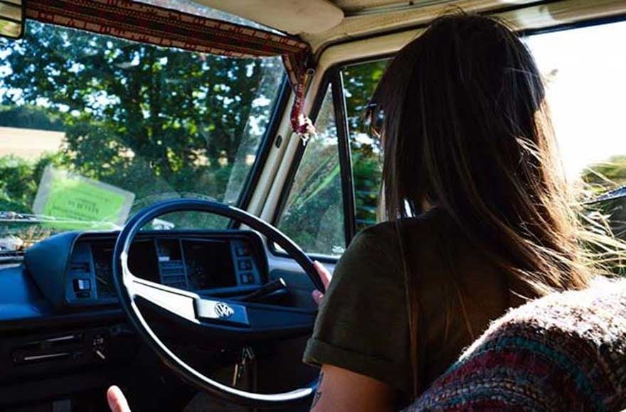 rear view view of a woman driving a campervan through a forest