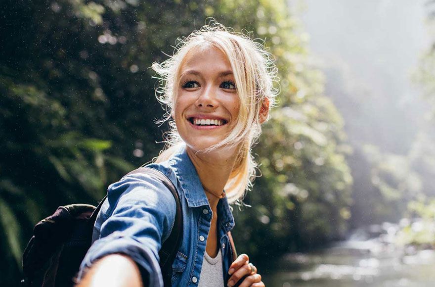 smiling woman wearing backpack exploring  a forest 