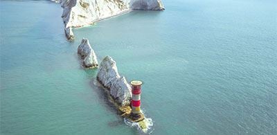 Red and white light house perched at the end of a row of islands 