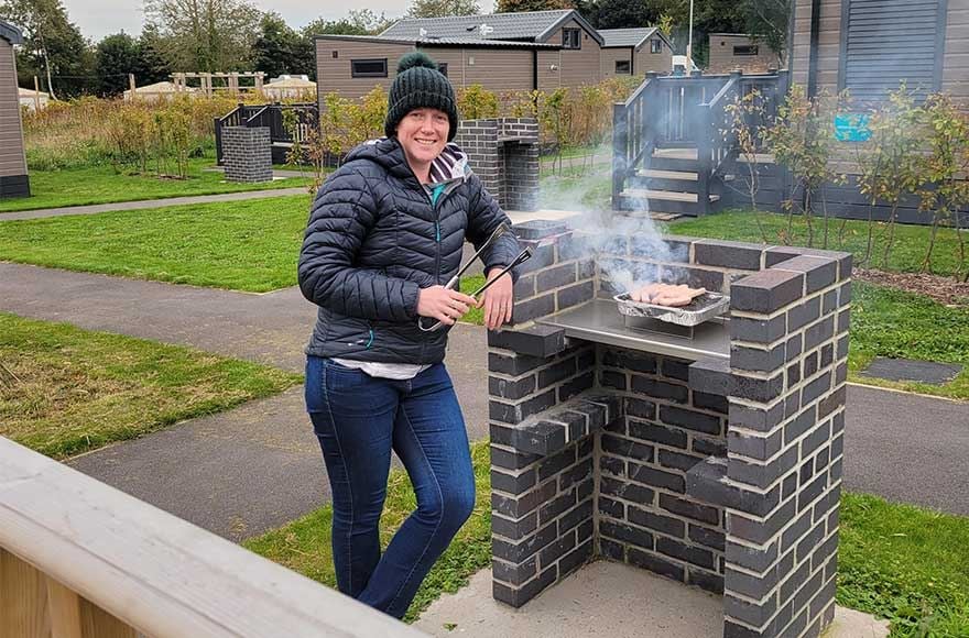 A woman poses next to a brick barbecue, highlighting an inviting outdoor space perfect for grilling and gatherings