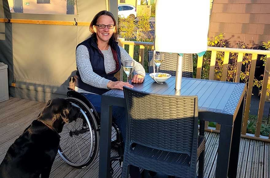 A woman in a wheelchair is seated at a table with a dog