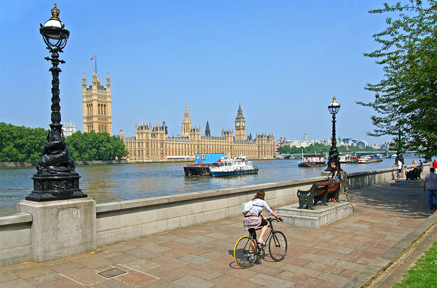 Lady cycling alongside the Thames, Palace of Westminster and boats in the background