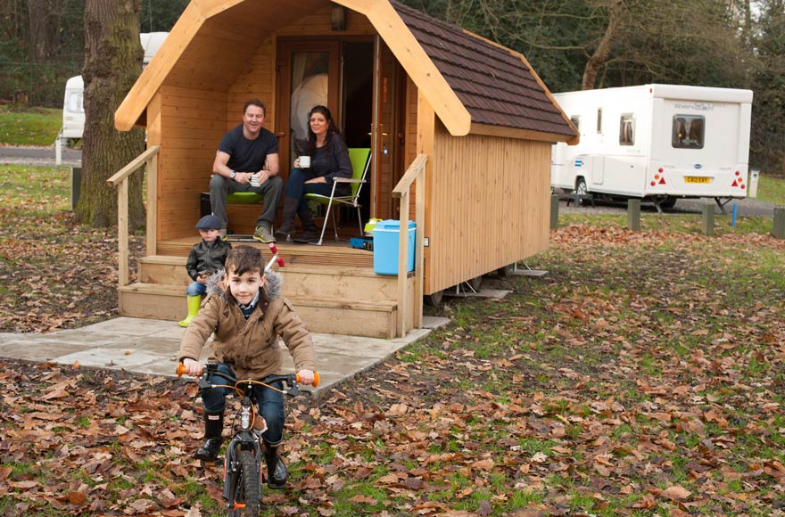 Child riding a bike while family watch from camping pod