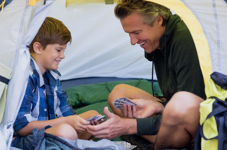 Father and son playing card game in their tent while it rains outside