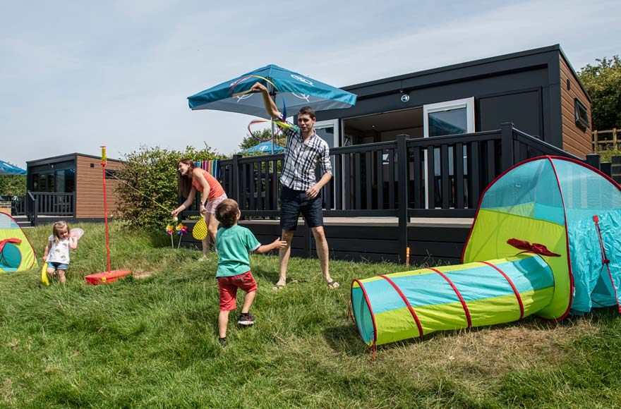 Family playing with swing ball and tent on grassy area outside glamping pod
